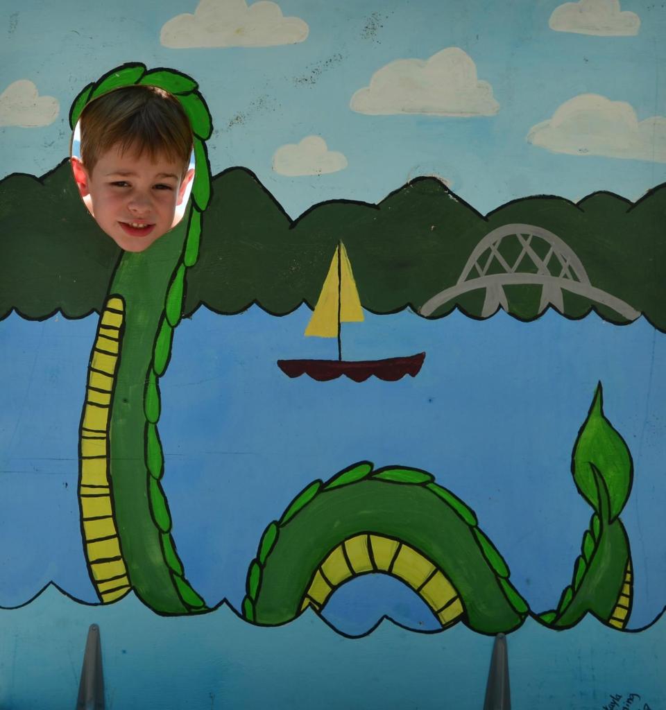 A small child pokes its face through a wooden display of Champ, the lake monster.