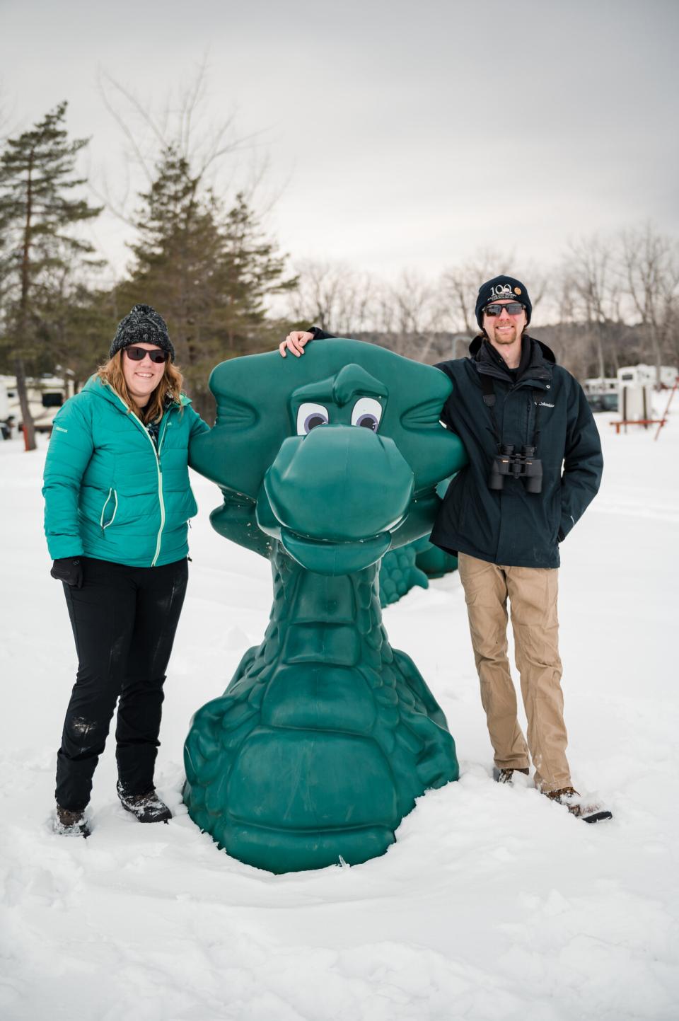 A man and woman pose next to a statue of a green lake monster.