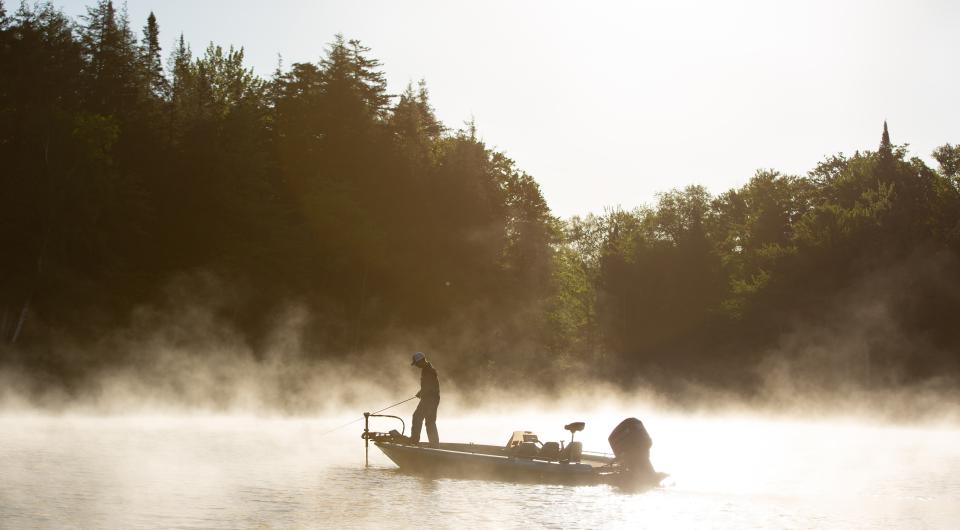 A angler fishing off a boat in the morning mist.