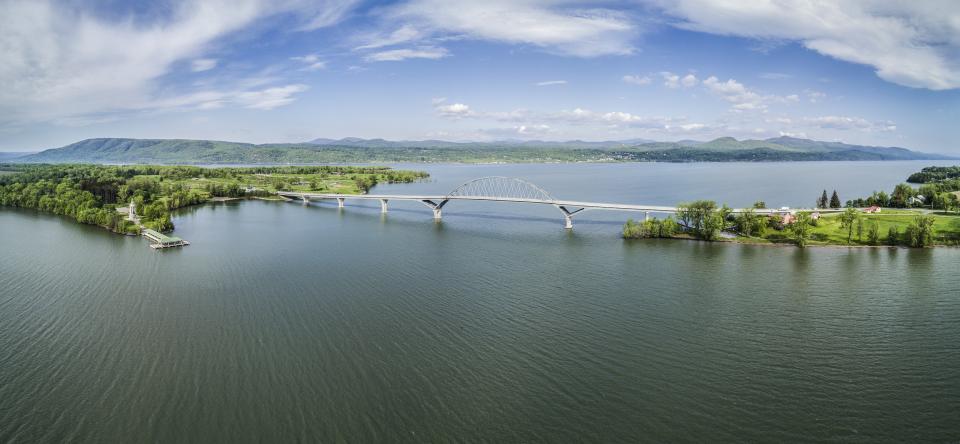 Birds eye view of the Champlain Bridge with lots of open water and distant mountains.