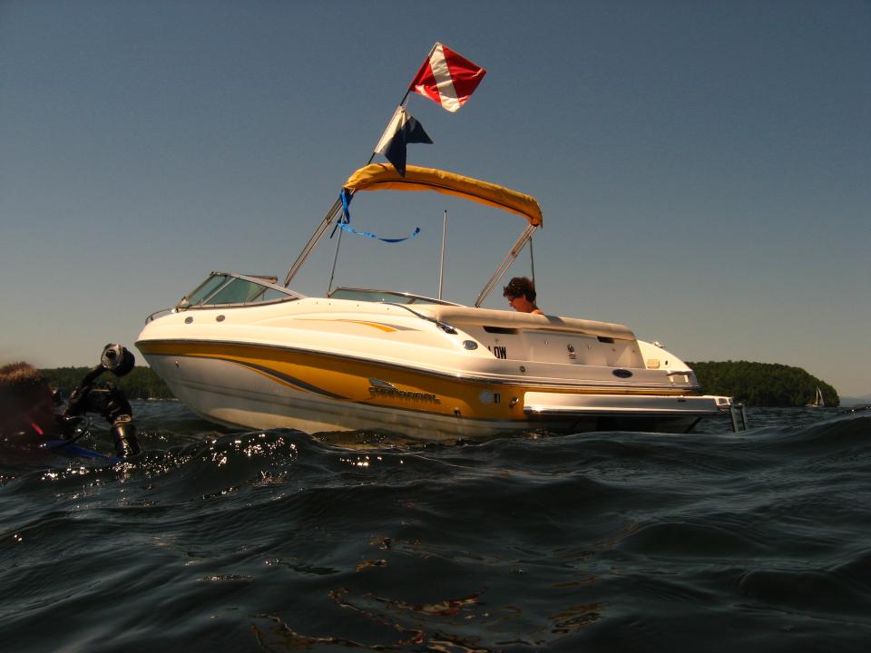 A white motorboat with diving flag aloft. A scuba diver floats in the water to the left of the boat. Image courtesy Gary Kessler.