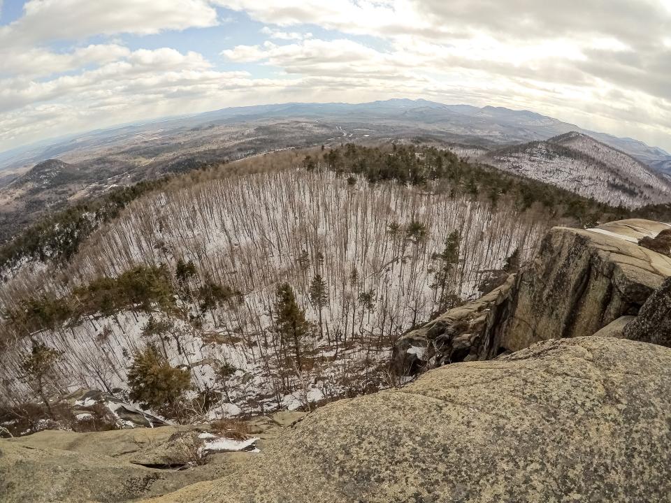 A wide angle looking down into a valley from a rocky mountain cliff.