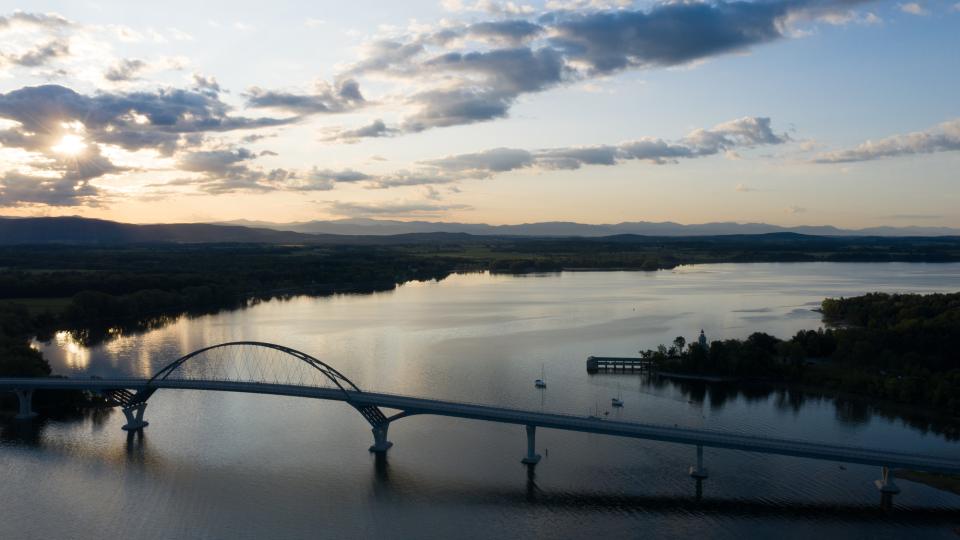 An aerial view of Lake Champlain with a bridge in the foreground and mountains in the background.