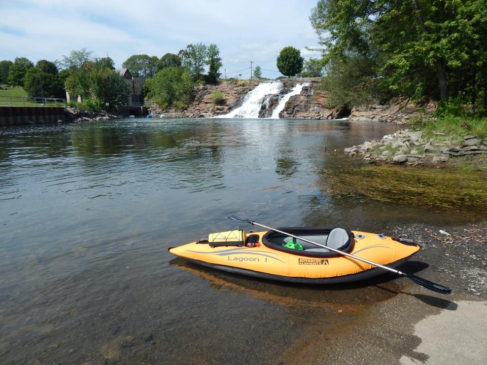 An inflatable kayak in front of the waterfalls on the LaChute River, with trees on either side and a dam.