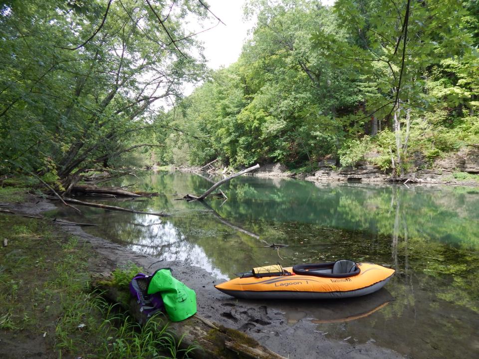 An orange kayak beached on a muddy bank on a river edged with thick trees.