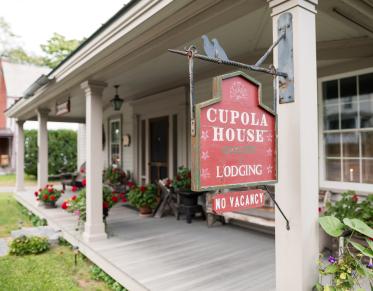 A red sign hanging off the post of a covered porch for Cupola House Lodging.