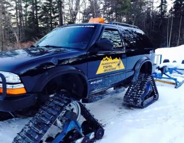 A modified SUV with tracks instead of wheels with a yellow decal for the Adirondack Trail Riders.