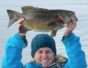 A person in a blue coat holds a fish over their head with joy.