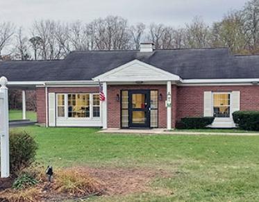A squat brick building with white trim and covered entry way with large lawn.