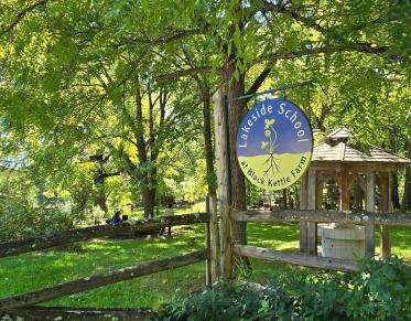 A lush green landscape where a round sign for Lakeside School at Black Kettle Farm.