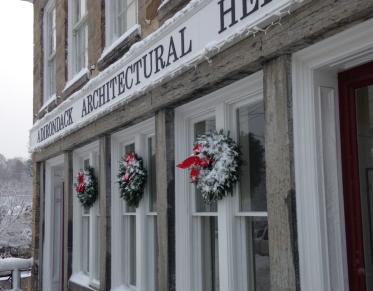 A tall stone building with white trim and winter wreaths with red bows that houses the Adirondack Architectural Heritage.