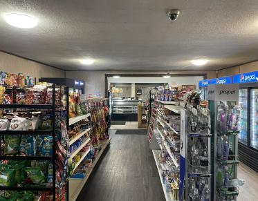Shelves of snacks and cold drinks in coolers leading to the deli counter at Grover Hills Deli