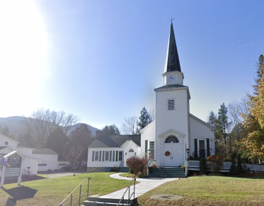 A white church with tall steeple and lush lawn.