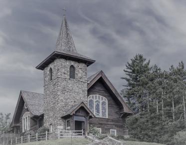 Tall stone steeple and wood church on top of a hill.
