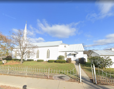 Exterior of the all white Immaculate Conception Church with tall arched windows and white wrought iron fence.
