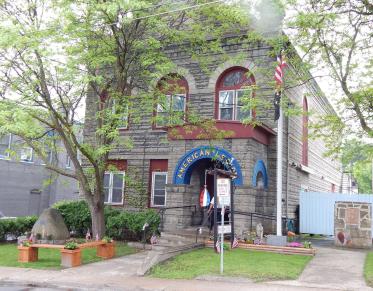 A grey stone building with red trim and a blue arched entry to the American Legion.