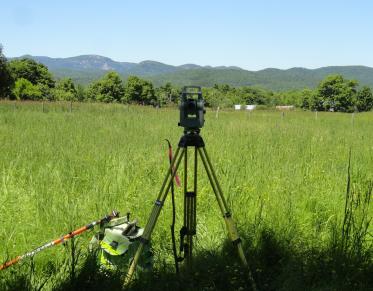 Survey equipment viewing a grassland with mountains in the background.