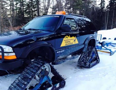 A modified SUV with tracks instead of wheels with a yellow decal for the Adirondack Trail Riders.