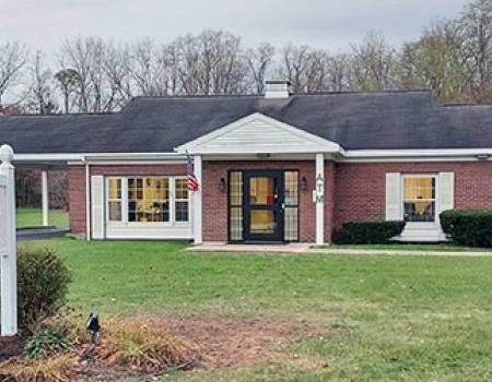 A squat brick building with white trim and covered entry way with large lawn.