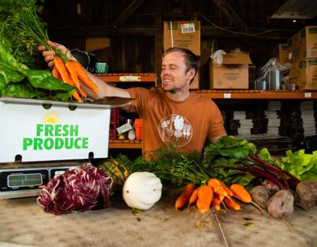 A man at a farm stand weighs a bundle of carrots.
