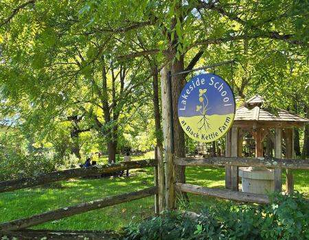 A lush green landscape where a round sign for Lakeside School at Black Kettle Farm.