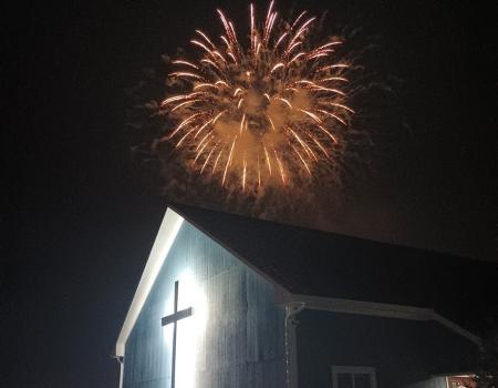 An illuminated cross on the side of a building with a firework exploding above.