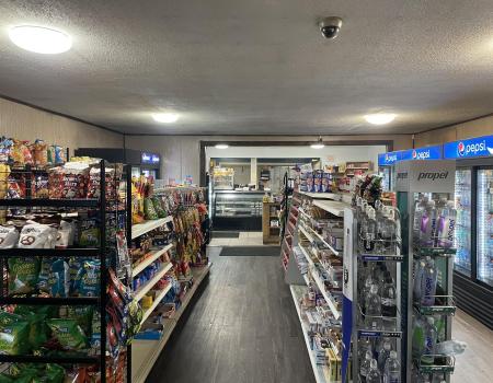 Shelves of snacks and cold drinks in coolers leading to the deli counter at Grover Hills Deli