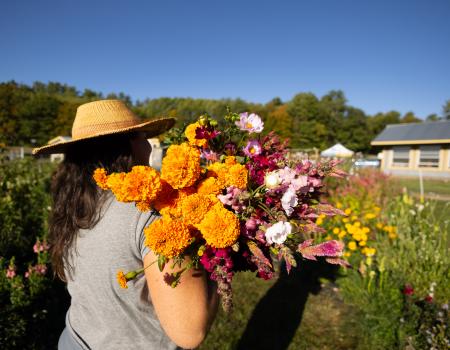 A woman in a straw hat holds a bouquet of orange and pink flowers over her shoulder.