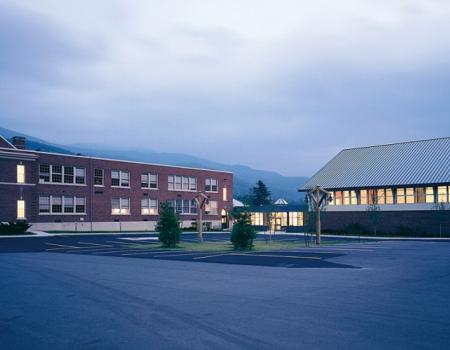 Brick school illuminated from within and surrounded by mountains.