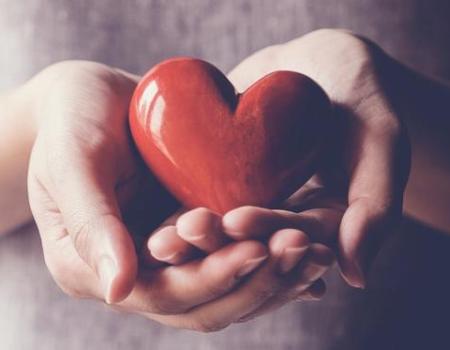 Hands holding a red heart shaped polished stone.
