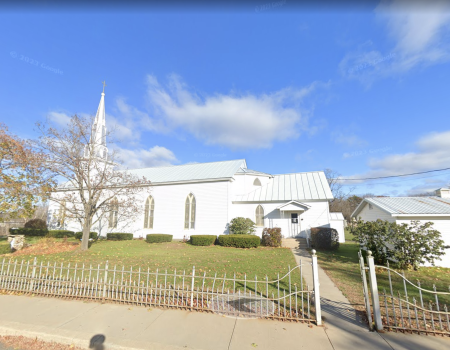 Exterior of the all white Immaculate Conception Church with tall arched windows and white wrought iron fence.