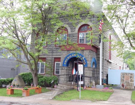 A grey stone building with red trim and a blue arched entry to the American Legion.