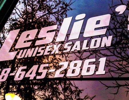 Window lettering at Leslies Unisex Salon reflecting a sunset.