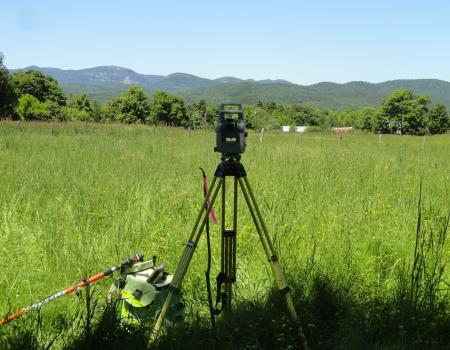 Survey equipment viewing a grassland with mountains in the background.