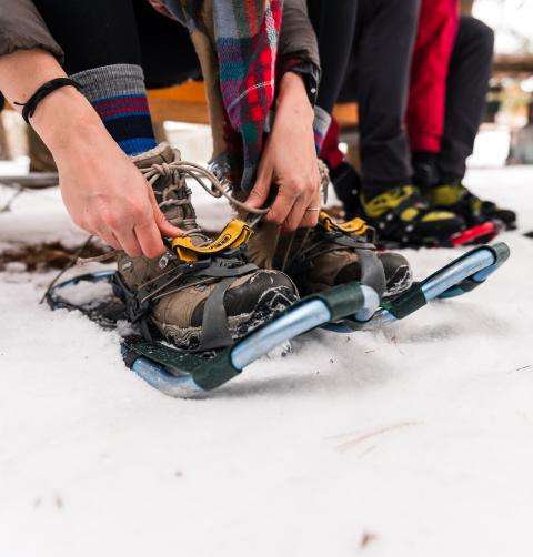 Two people strap on snowshoes