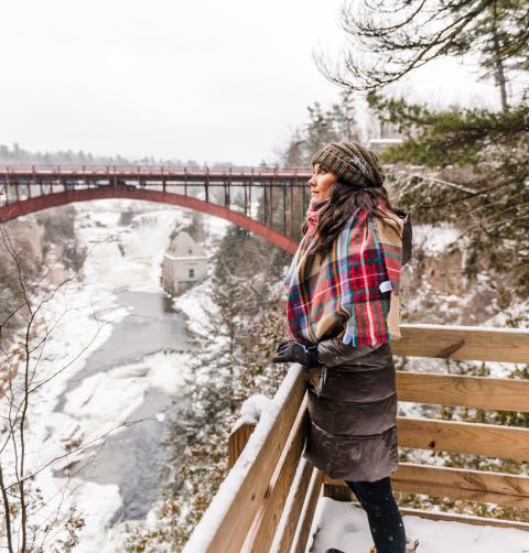 A woman overlooks a chasm with a bridge running over it during the winter.