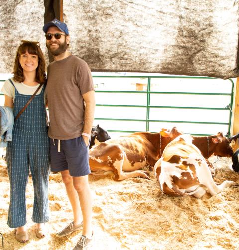 A man and woman stand proudly by their sleeping cattle. 
