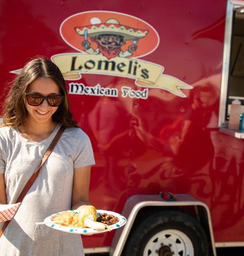 A woman holds two paper plates of food in front of a food truck. 