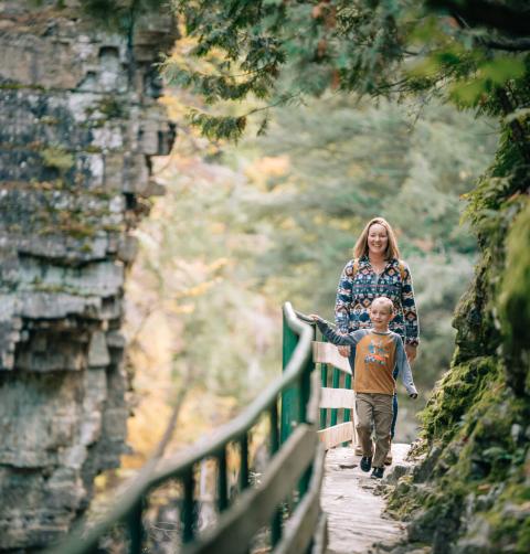 A woman and her young son walk on a nature path at a waterfall.