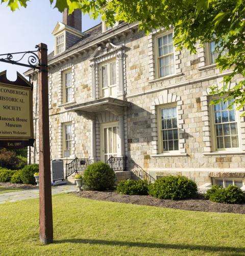 The exterior of a historic stone 2-story home in the Federal style. A sign on the lawn indicates it is a museum.