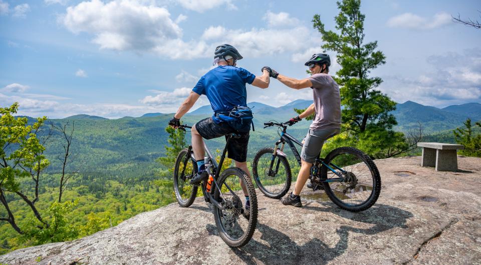 Two mountain bikers fist bump at an overlook