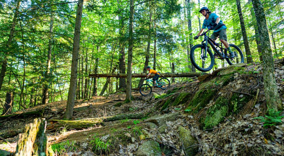 A mountain biker rides down a steep rocky section of trail in the woods