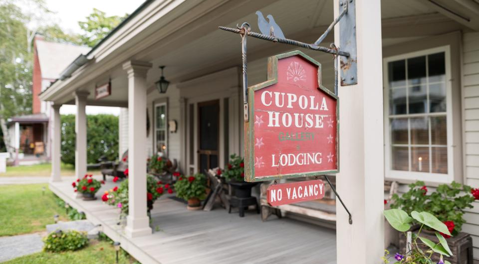 A red sign hanging off the post of a covered porch for Cupola House Lodging.