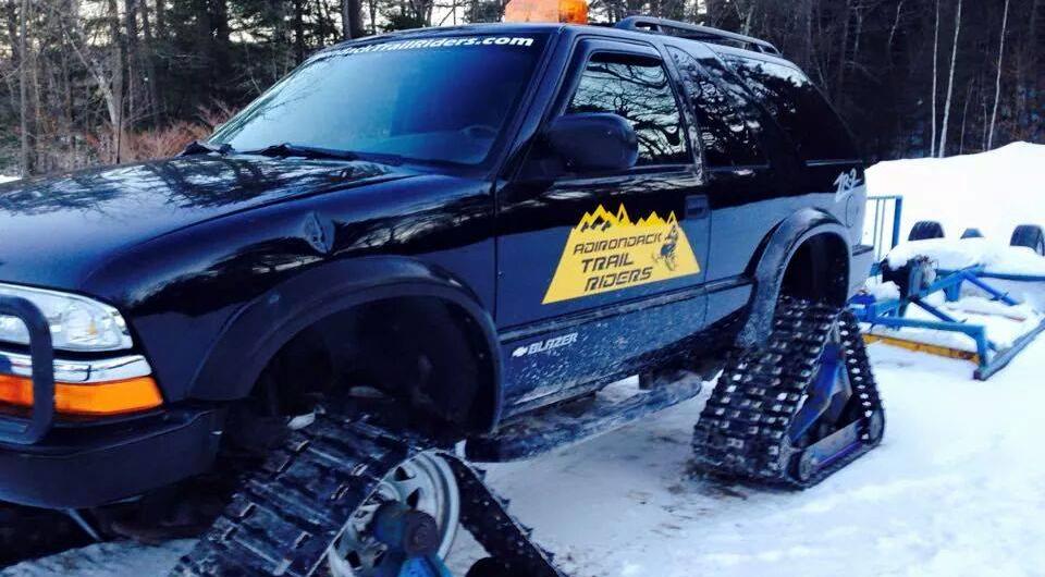 A modified SUV with tracks instead of wheels with a yellow decal for the Adirondack Trail Riders.