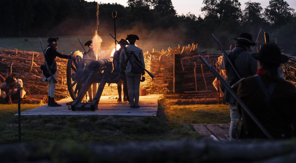 Reenactors cook a meal over a fire