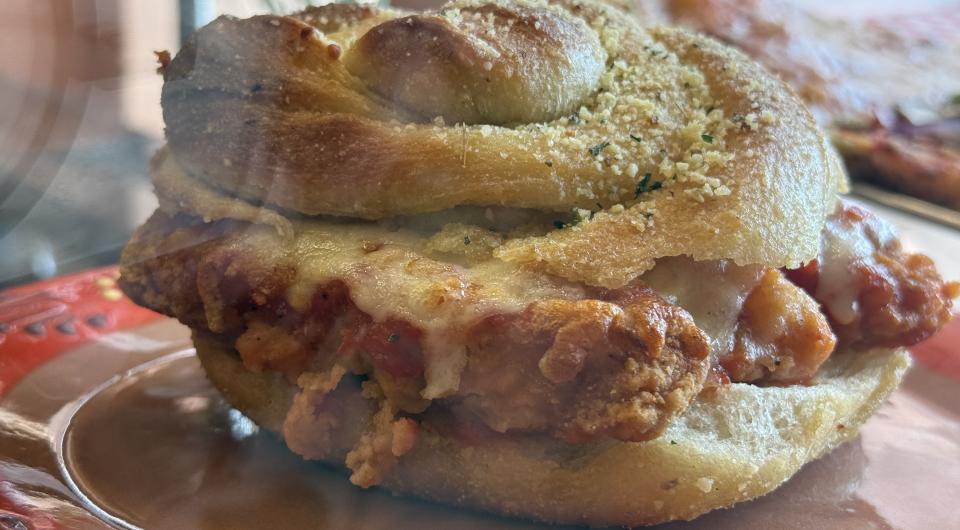 A chicken cutlet with cheese and sauce on a  giant garlic knot sandwich.