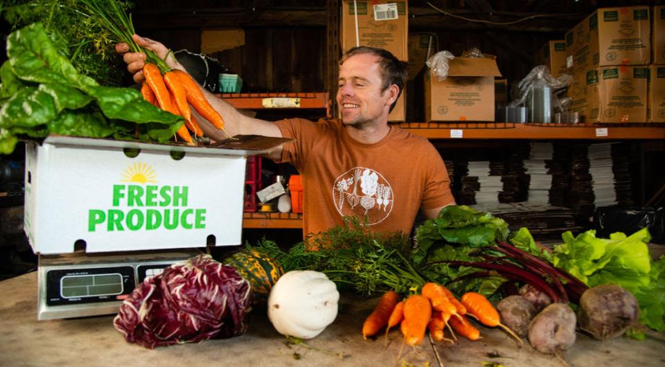 A man at a farm stand weighs a bundle of carrots.