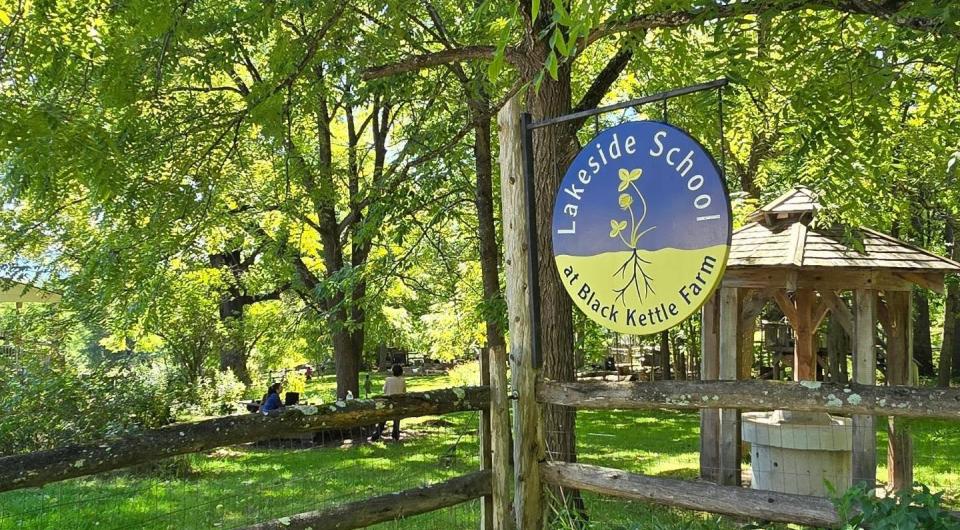 A lush green landscape where a round sign for Lakeside School at Black Kettle Farm.