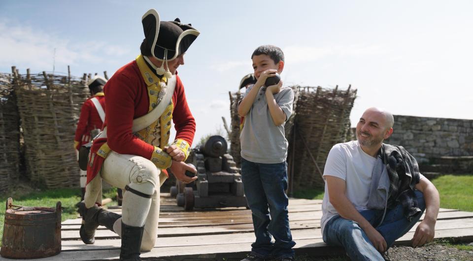 A reenactment performer in redcoat attire speaks with a young child.