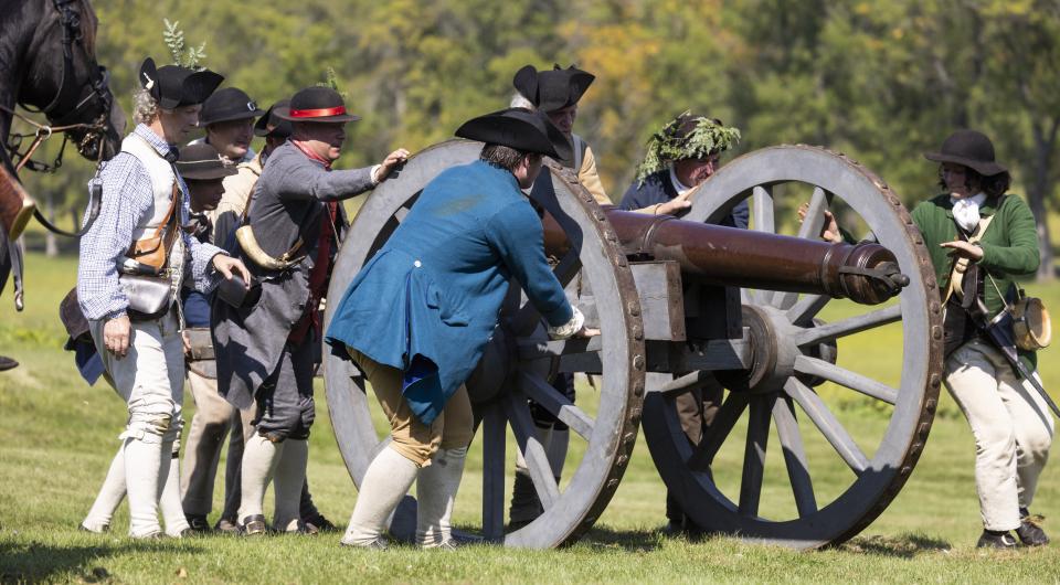 Reenactment actors in period correct clothing demonstrate a cannon firing.